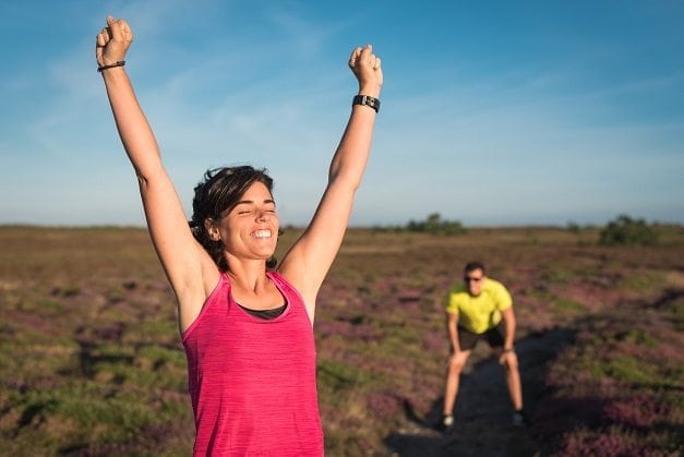 Smiling runner woman rising her arms after wining trail running